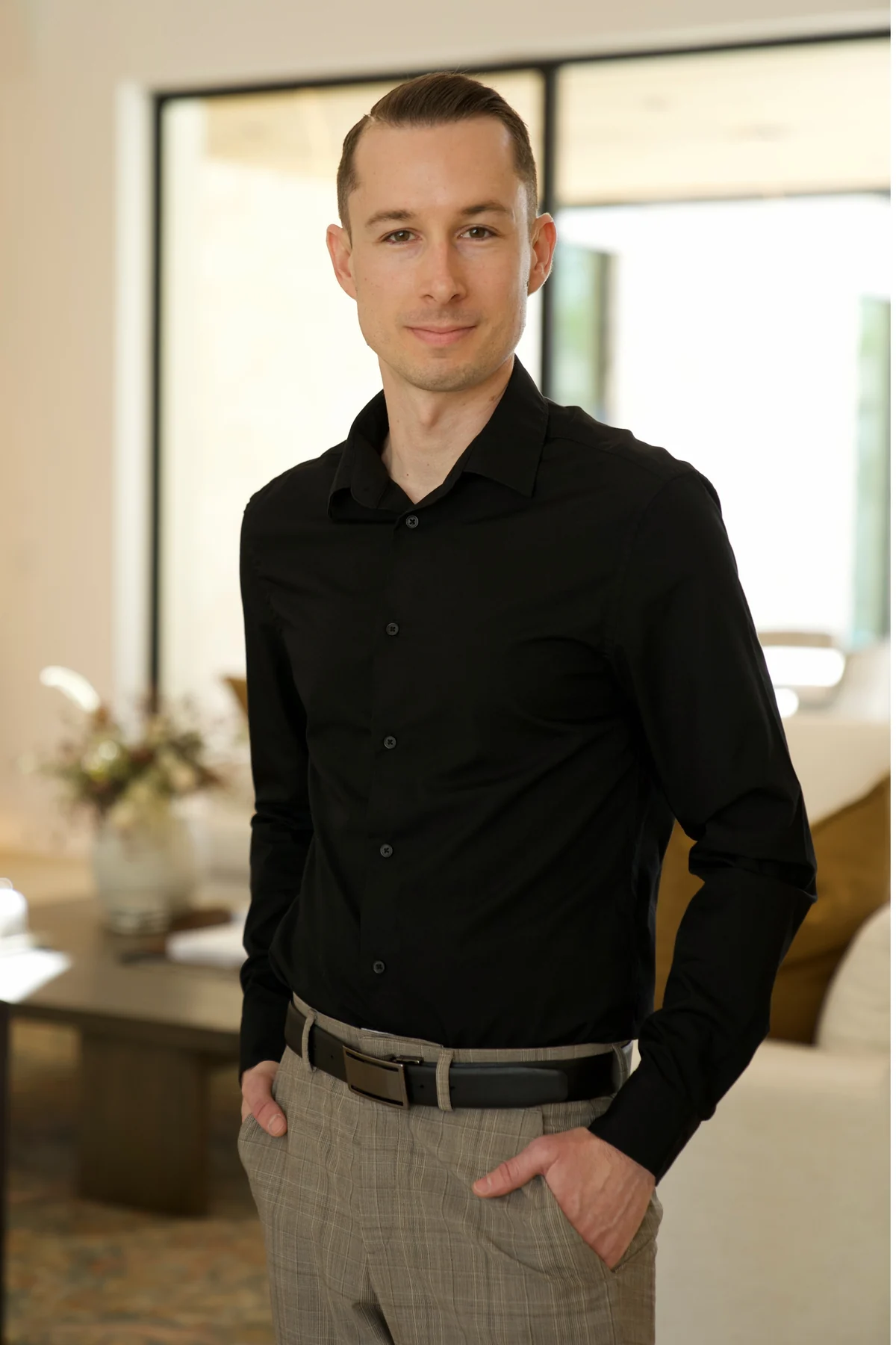 Justin Taylor standing in a black shirt beside a sunlit window